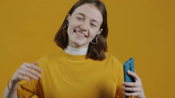 Slow Motion Portrait of Happy Lady Wearing Earpods and Holding Smartphone Dancing on Yellow