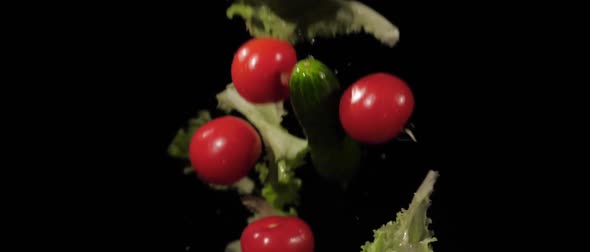 Tasty Wet Tomatoes Cucumbers and Lettuce Tossed Up and Fly Around on a Black Background in Slow