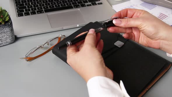 Business woman hands closing a pen near agenda and laptop close up