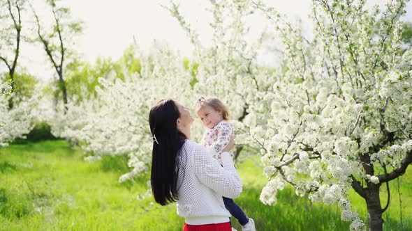 Mom Throws Up Her Daughter in the Park By a Flowering Tree