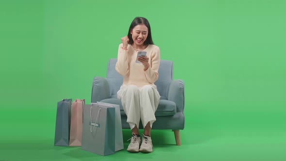 Front View Of Happy Asian Shopping Woman With Shopping Bags Using Mobile Phone On Green Screen