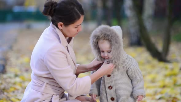 mother carefully fastens clothes to her little daughter on the street in the autumn evening