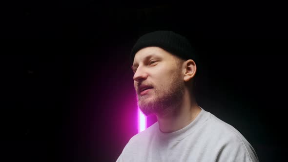 Side View of a Young Man in a Black Cap Talking and Giving Interview Against Black Background