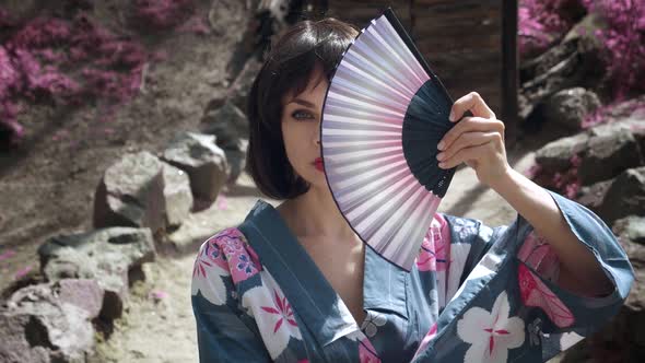 Closeup of Caucasian Geisha Woman in Traditional Japanese Kimono is Covering Her Face with Wooden