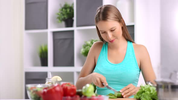 Enthusiastic Young Housewife Chopping Cucumber Cooking Vegetable Salad in Kitchen at Home