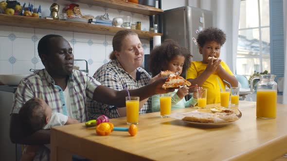 Multiethnic Family with Three Children Eating Pizza Indoors in Kitchen