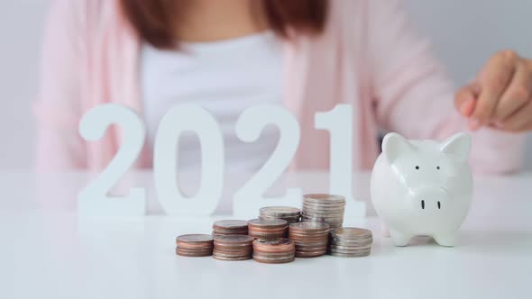 Stack of coins with young woman putting coin into the piggy bank