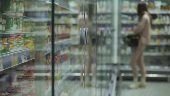 Young Woman Walking Down the Aisles of a Supermarket with a Basket of Groceries