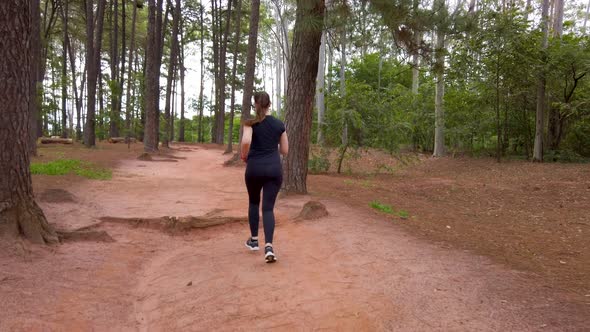 Girlrunning on a dirt trail between trees, camera following the subject from behind.