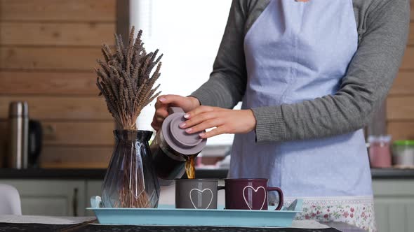 Young Woman Pouring Hot Tea Into Mugs in Kitchen