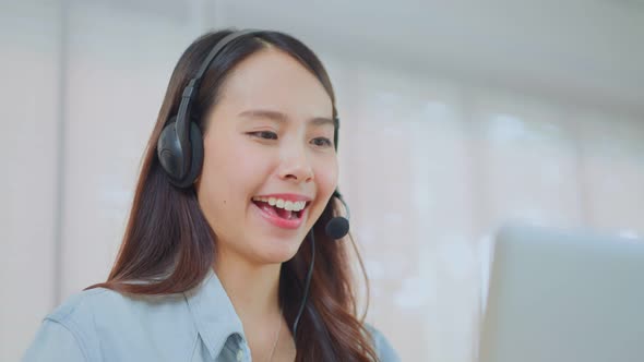 Asian Telemarketing or call center with headset talk and working on computer lap top at home office.
