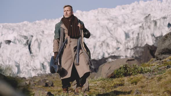 Man In Greatcoat Carrying Guitar Case And Bag Away From Glacier