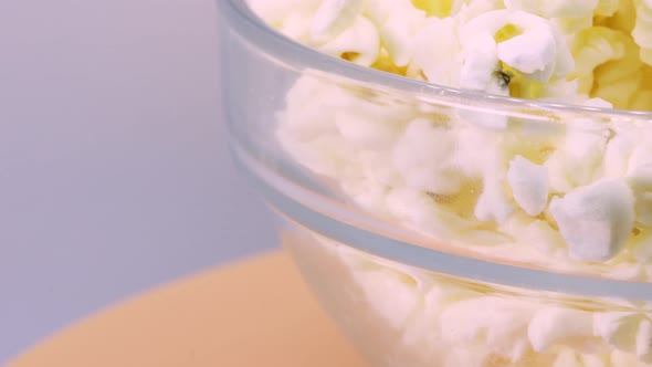 Extreme close up of popcorn in transparent glass bowl rotating on orange surface, macro shot view in