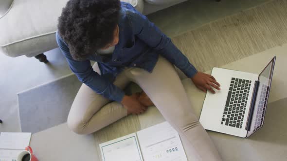 Happy african american woman sitting on floor, using laptop and working