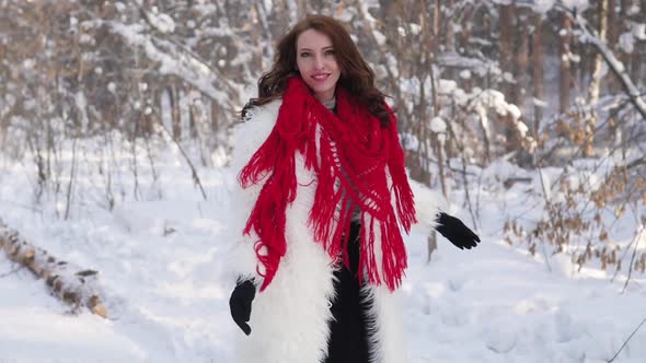 Attractive Blonde in a White Fur Coat and Red Scarf Posing on the Background of a Winter Forest