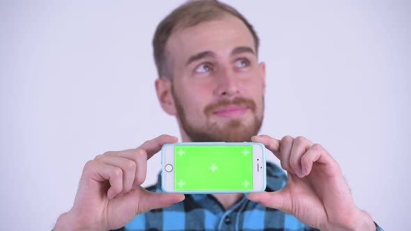 Face of Happy Bearded Hipster Man Thinking While Showing Phone