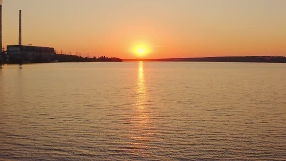 Beautiful sunset over the river. Silhouette of industrial plant near the evening water. 