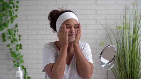 Portrait of young woman applying cream in front of mirror