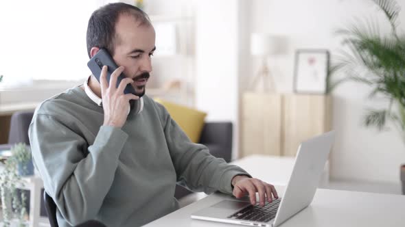 Mid Adult Man Talking on Mobile Phone While Working on Laptop From Home Office