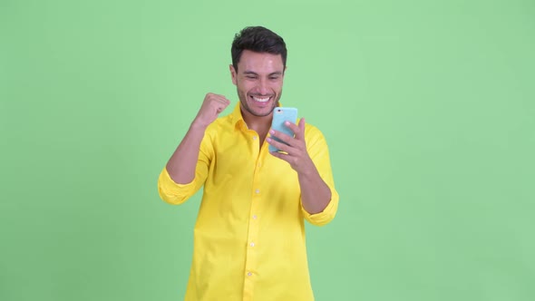 Happy Young Hispanic Businessman Using Phone and Getting Good News