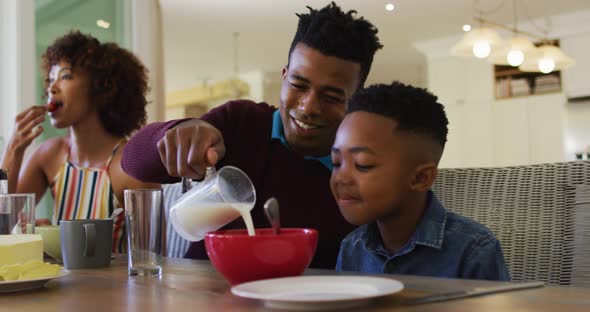 African american father smiling while pouring milk in cereal bowl on his son at home