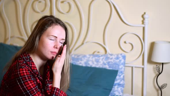 Young sleepy woman is trying to wake up sitting in bed