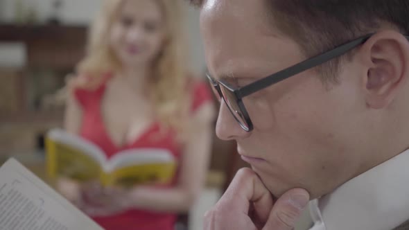 Young Concentrated Man in Glasses Reading the Book in the Foreground While Pretty Blond