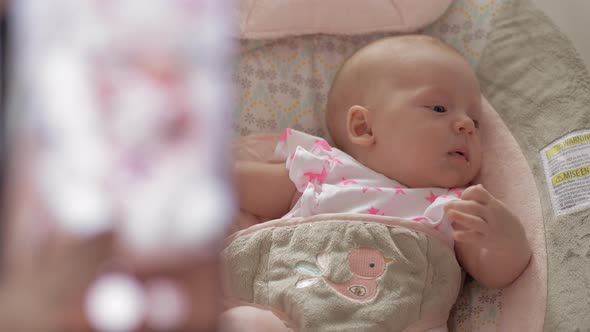 Mother taking mobile photo of baby daughter in bouncy seat