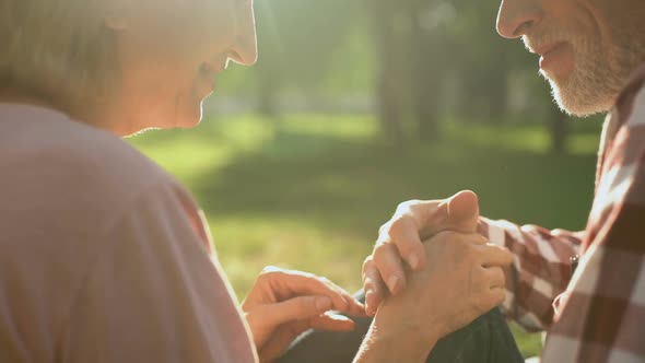 Male Pensioner Tenderly Holding Female Hand on Romantic Date in Park, Closeup