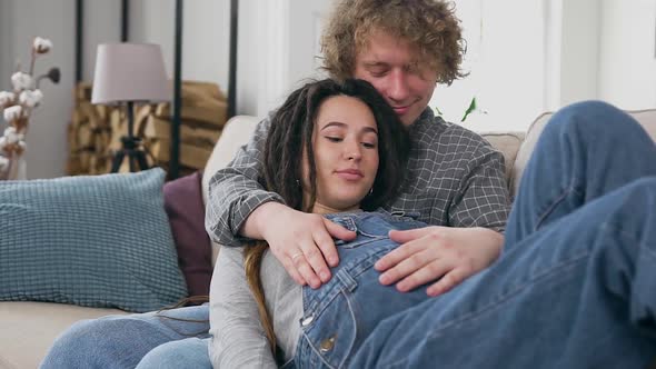 Man Holding in His Huggs Pregnant Smiling Wife and Tenderly Touching Her Tummy