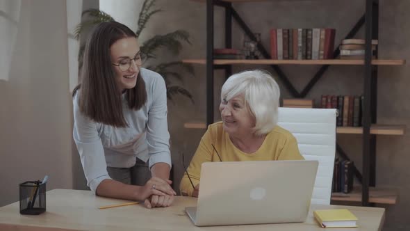 Young Woman Teaches an Senior Funny Woman to Use a Laptop