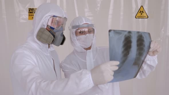 Two Doctors in Medical Protective Suits Examine a Chest X-ray in a Hospital Room