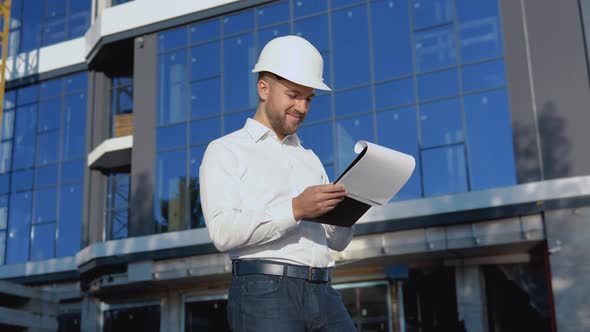 Engineer Architect in a White Shirt and Helmet on the Background of a Modern Glass Building Works