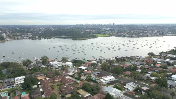 Flying over neighborhood town with residential homes and houses with boat marina in the background.