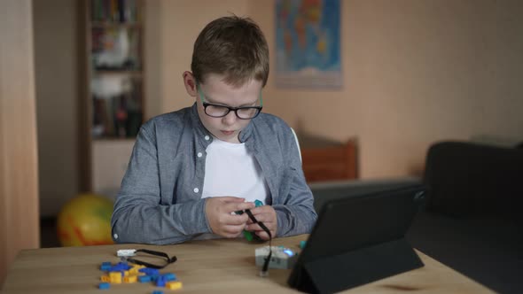 Boy in Glasses is Assembling His Own Model of Robot From Constructor on Table