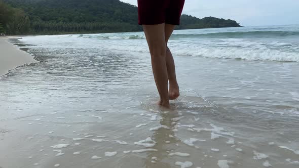 walking along sea water waves on sandy beach. Pretty woman walks at seaside surf.