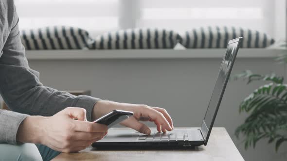 Man Using Smartphone and Laptop Connected to Work and Searching Information at Office