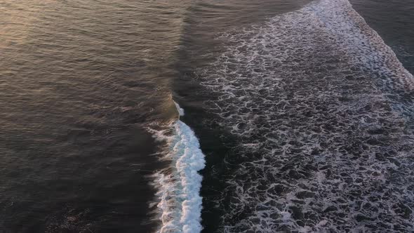 Beautiful foamy waves rolling on the sandy beach in Bali, during the sunset. Slow motion aerial shot