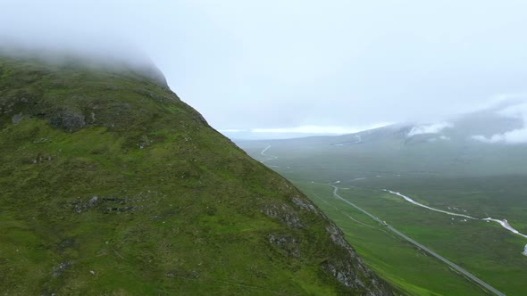 Pan shot of mountain reveals long picturesque road in Scottish highlands