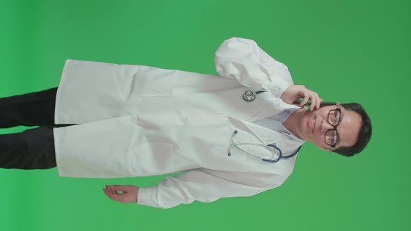 Asian Doctor With Stethoscope Talking On Mobile Phone While Walking On Green Screen