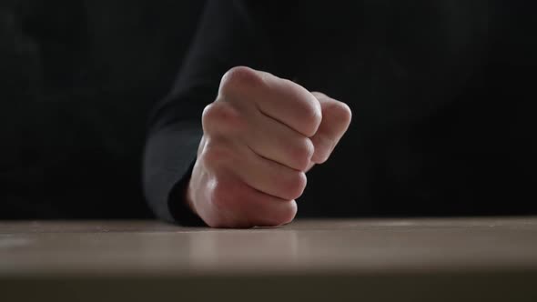 Close Up Man Beats His Fist on the Table Showing Aggression on Dark Background