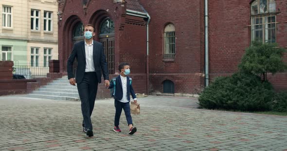 Young Man in Suit Holding Hand in Hand with His Son Carrying Bag While They Wearing Protective Masks