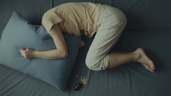 A Young Woman Lies on the Bed with Her Head Under the Pillow