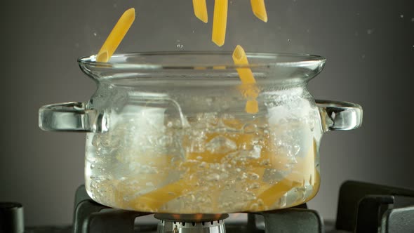 Super Slow Motion Shot of Fresh Penne Falling Into Boiling Salted Water 