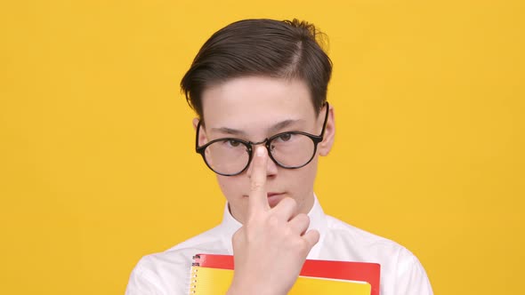 Schoolboy Adjusting Eyeglasses Holding Books Posing Over Yellow Background