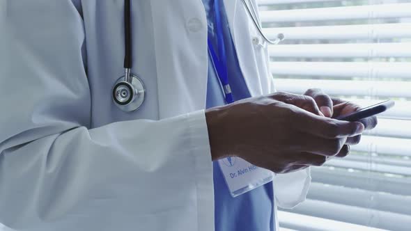 Mid section of African American male doctor using mobile phone in hospital 