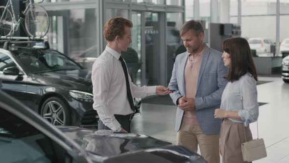 Salesman Handing Car Keys to Couple in Dealership