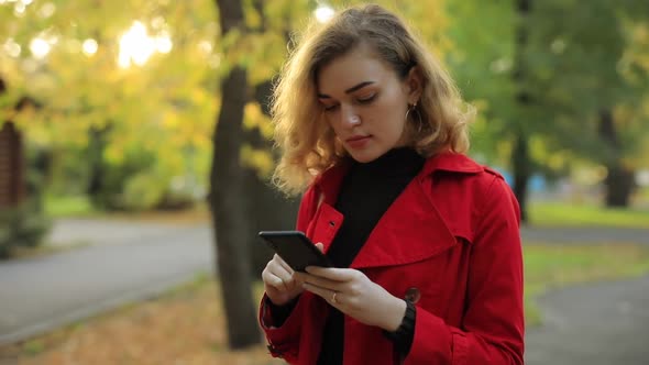 Beautiful Woman Looks Down Into Smartphone at the Fall Day