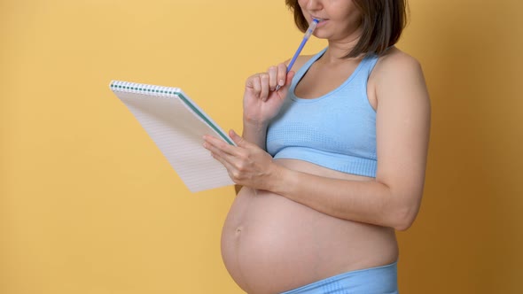 a Pregnant Woman with a Notebook and a Pen Chooses a Name for the Unborn Child and Writes Her Plans