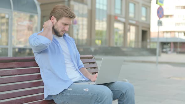 Man with Neck Pain Using Laptop While Sitting Outdoor on Bench
